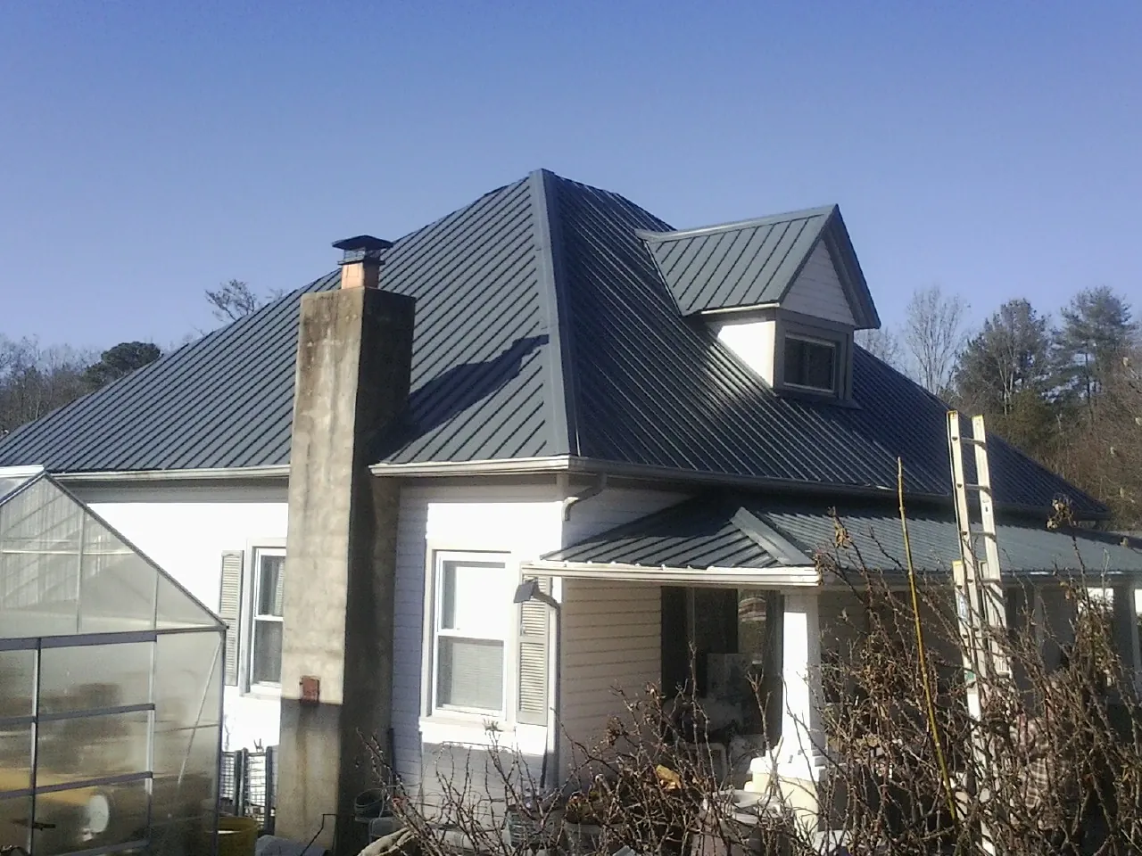 Dark blue standing seam metal roof on a white farmhouse with dormer — Slate & Tile Roof Repair by Roofing Brothers in Fair Oaks