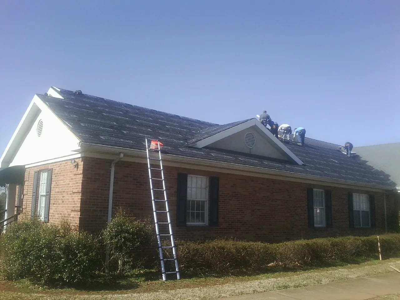 Crew tearing shingles off a brick ranch roof with a ladder set — Emergency Roof Repair work by our crew in Fair Oaks