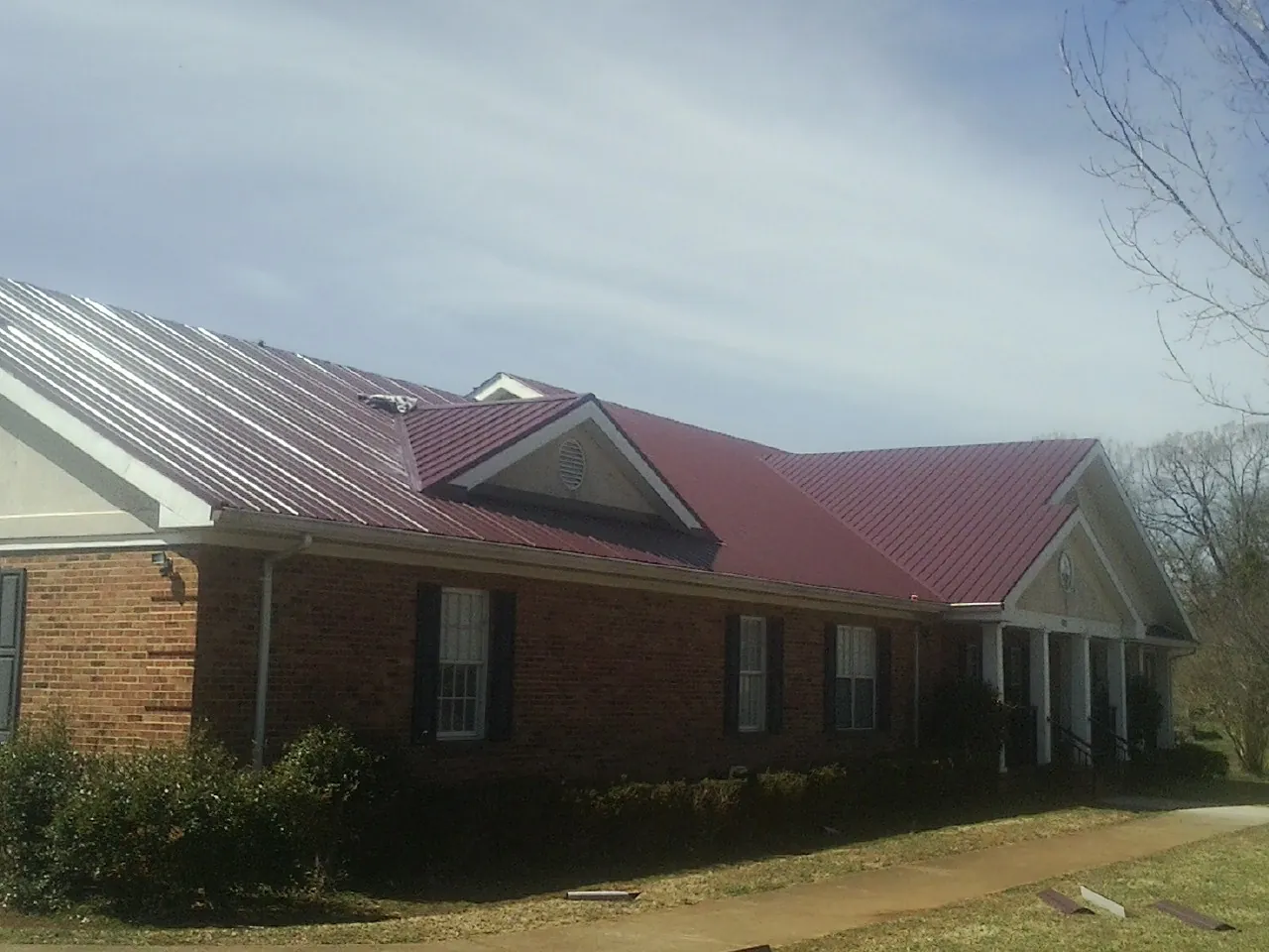 Red metal roof with gabled entries on a long brick building, from a Hail Damage Roof Repair job in Fair Oaks