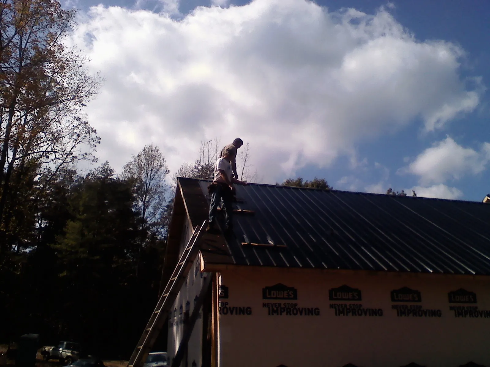 Roofer fastening dark metal panels high against a cloudy sky, from a Roof Inspection job in Fair Oaks