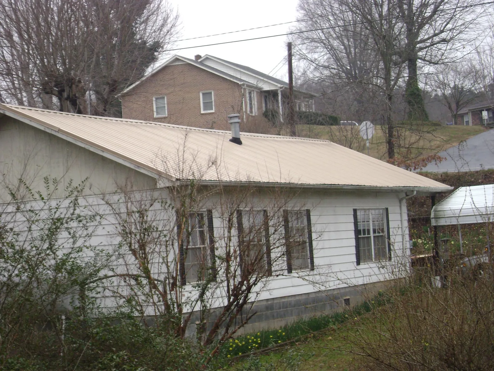 Tan metal roof on a white sided house set into a hillside — Commercial Roofing by Roofing Brothers in Fair Oaks